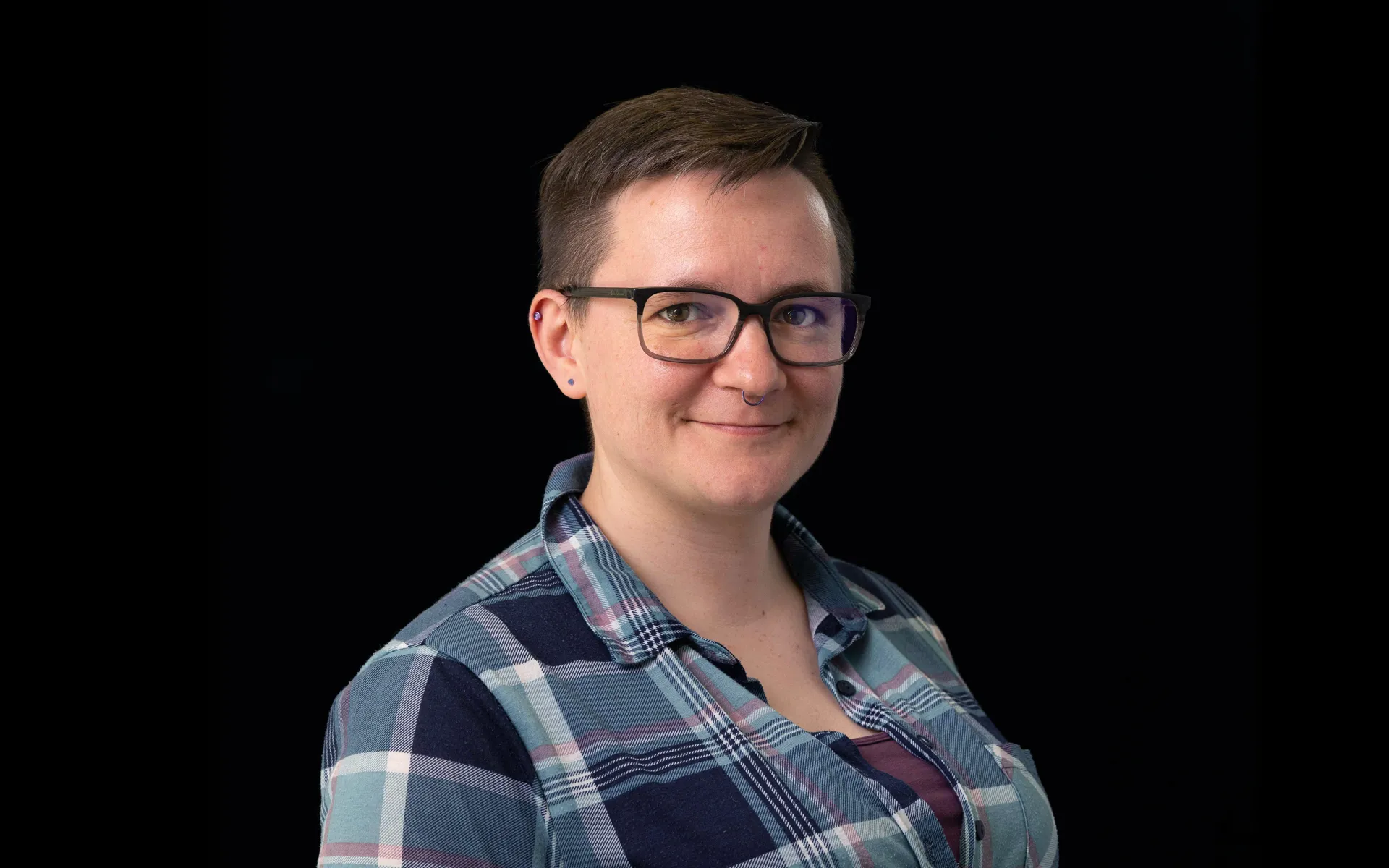 Portrait of Heather McCready wearing glasses and a blue checked shirt against a black background.