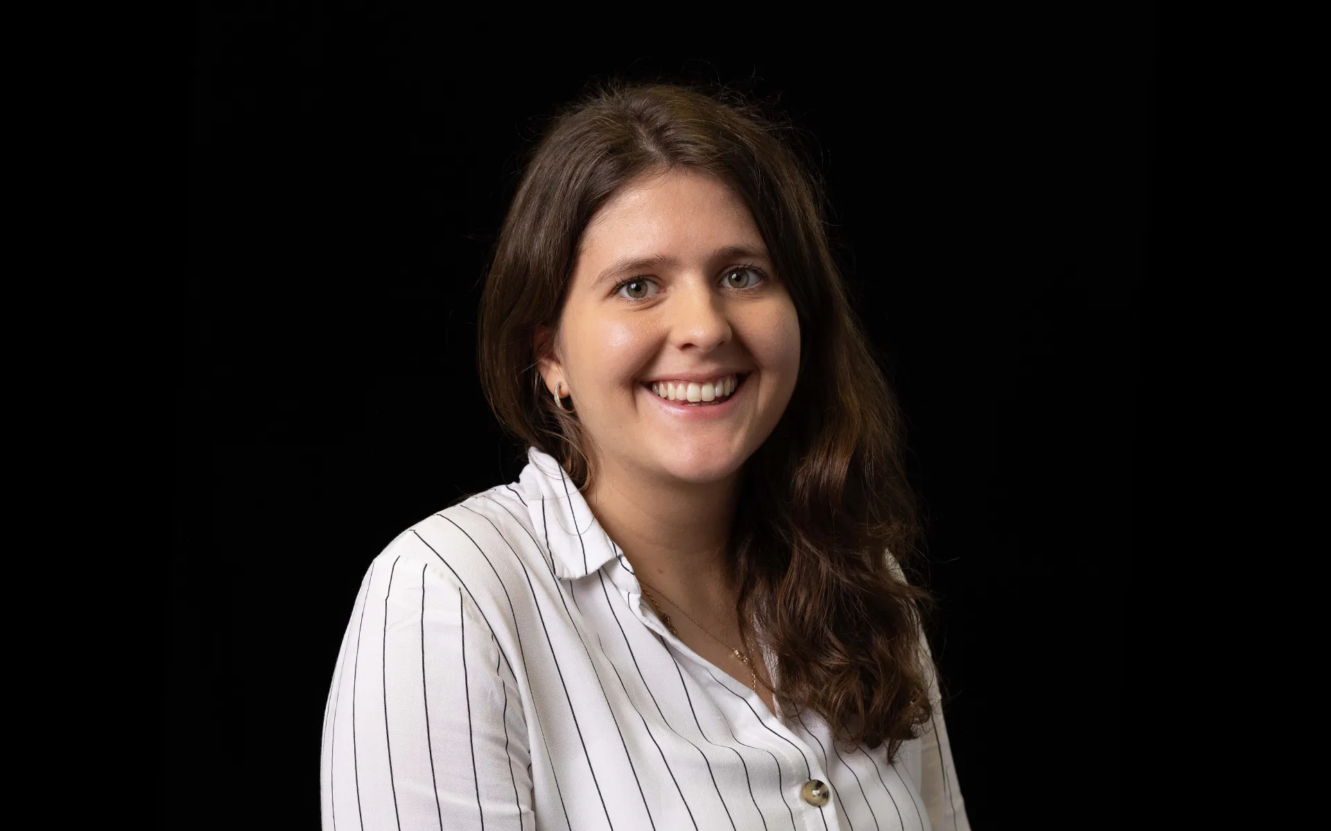 Portrait of Holly Frost wearing a white striped shirt against a black background.