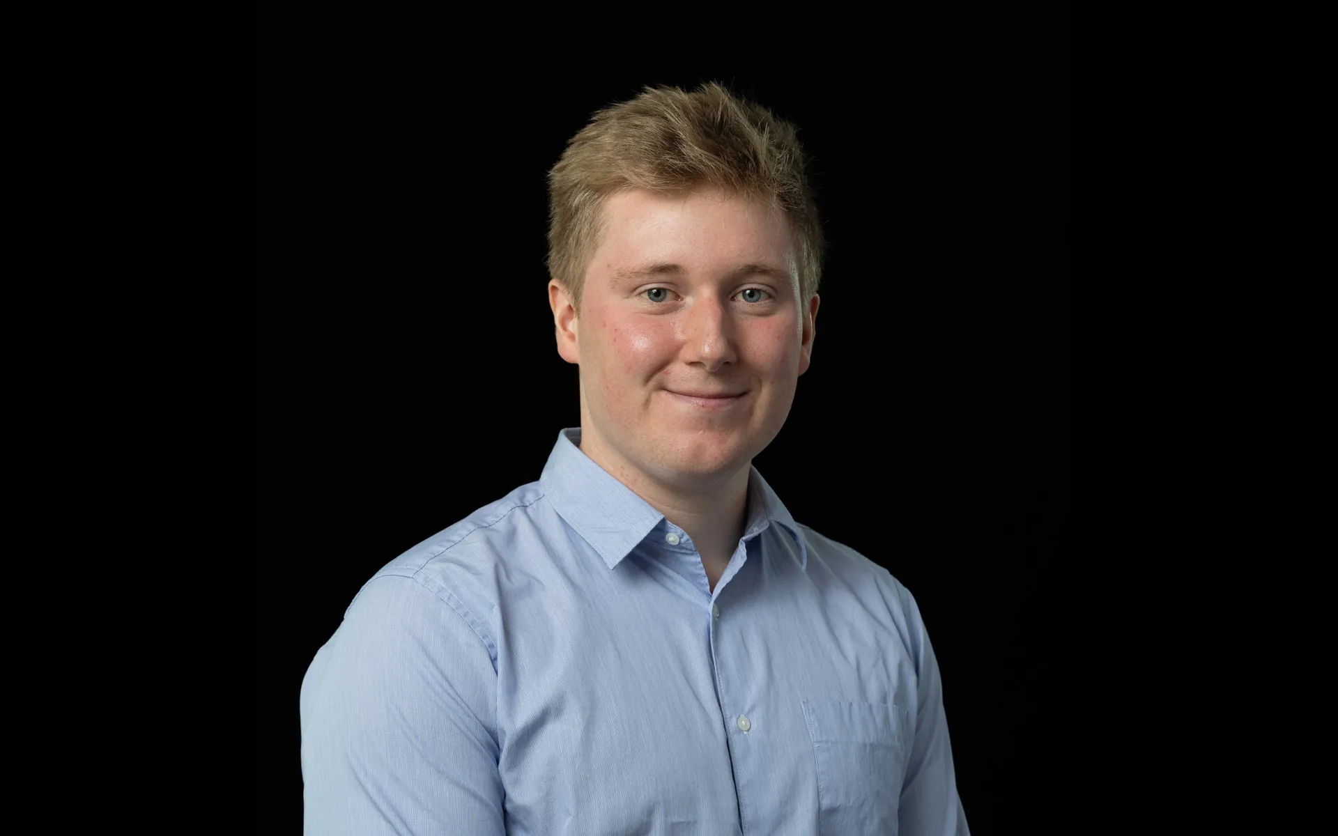 Portrait of Iain Nethercote wearing a light blue button-up shirt and glasses against a black background.