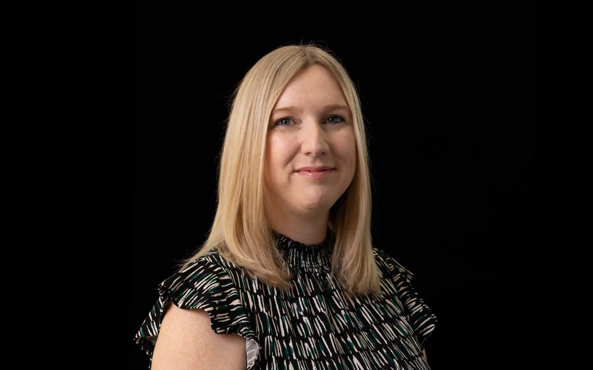 Portrait of Jacqueline Murray wearing a patterned black top against a black background.