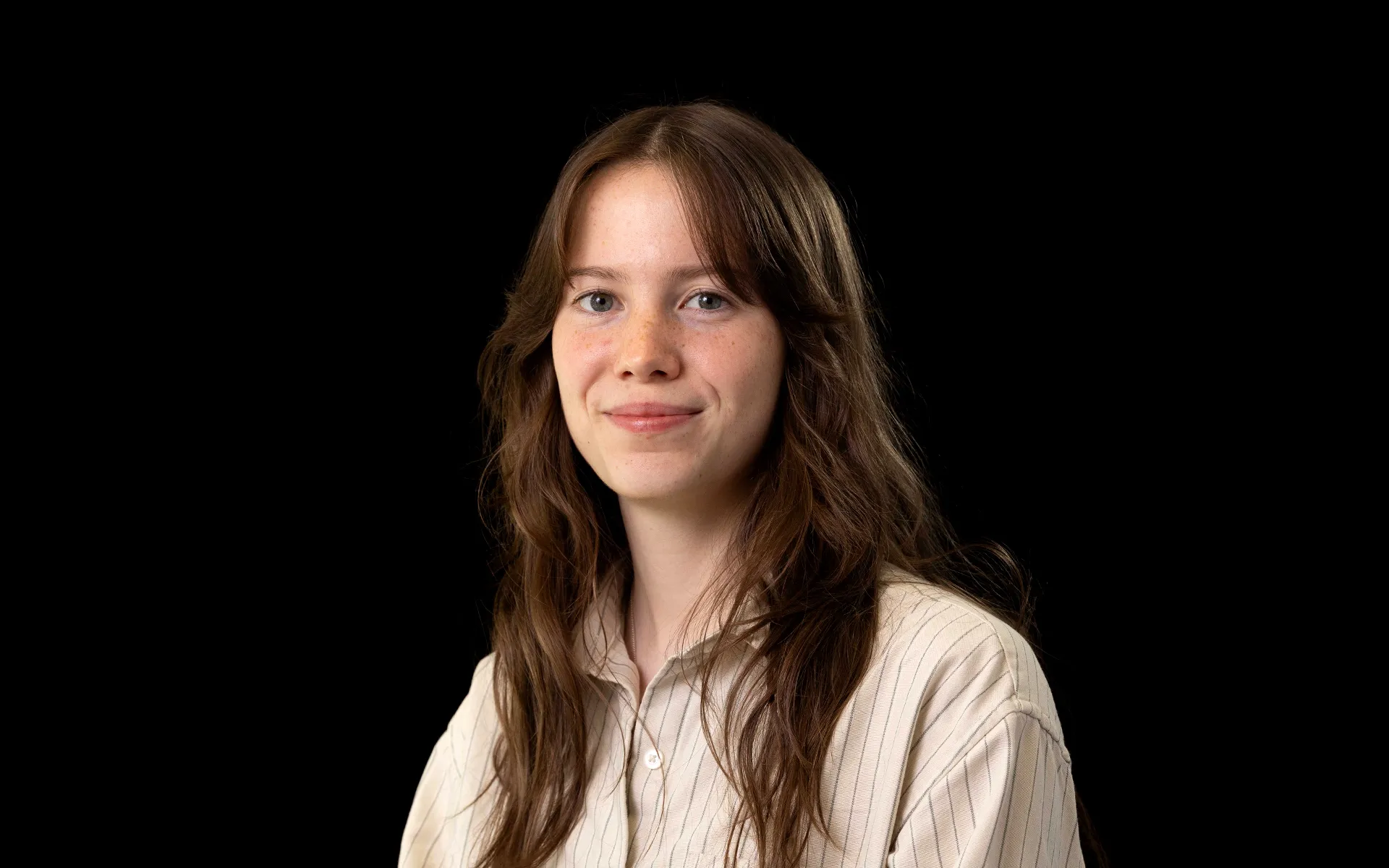 Portrait of Mia Howie wearing a light olive-green shirt against a black background.