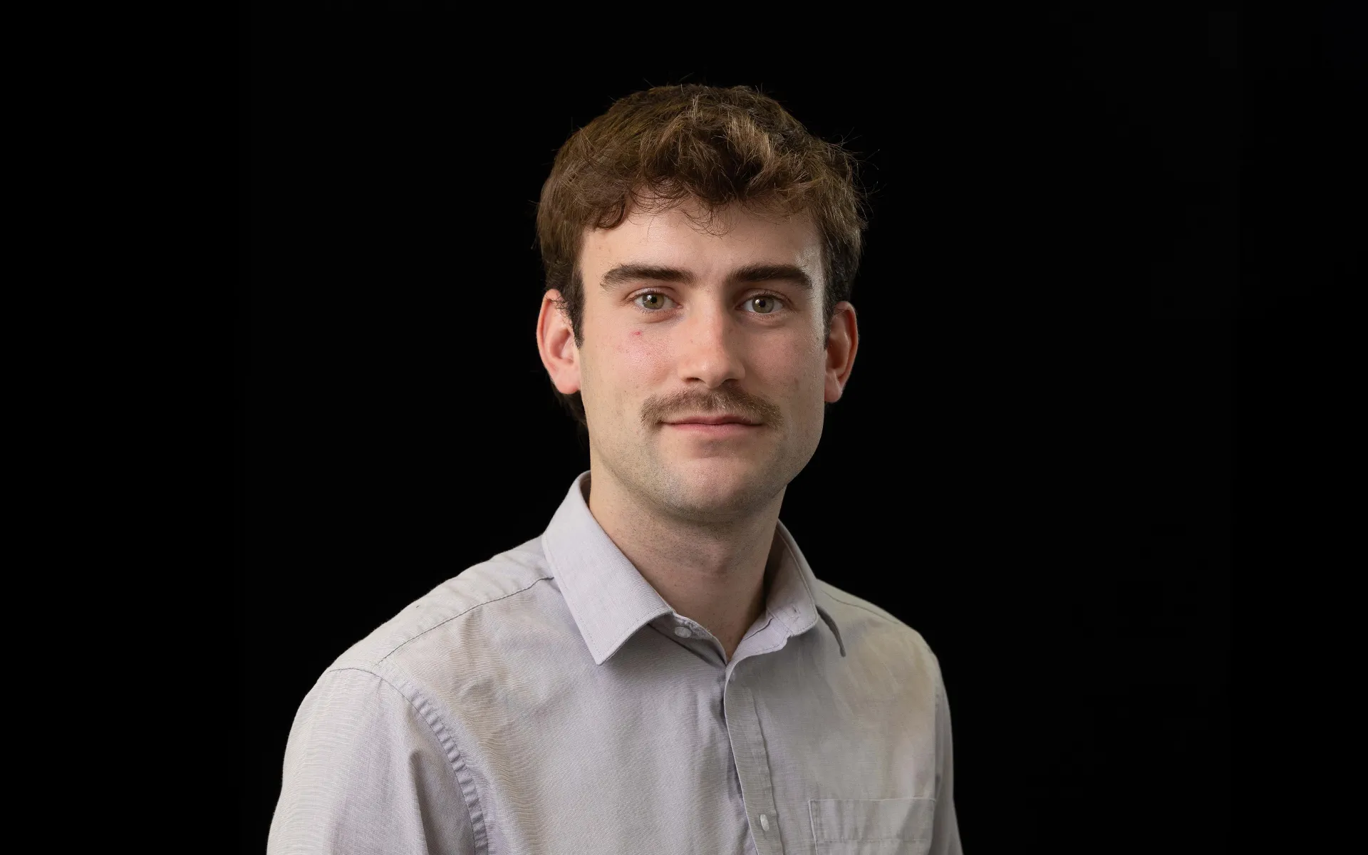 Portrait of Reece Menzies wearing a white high-neck top against a black background.