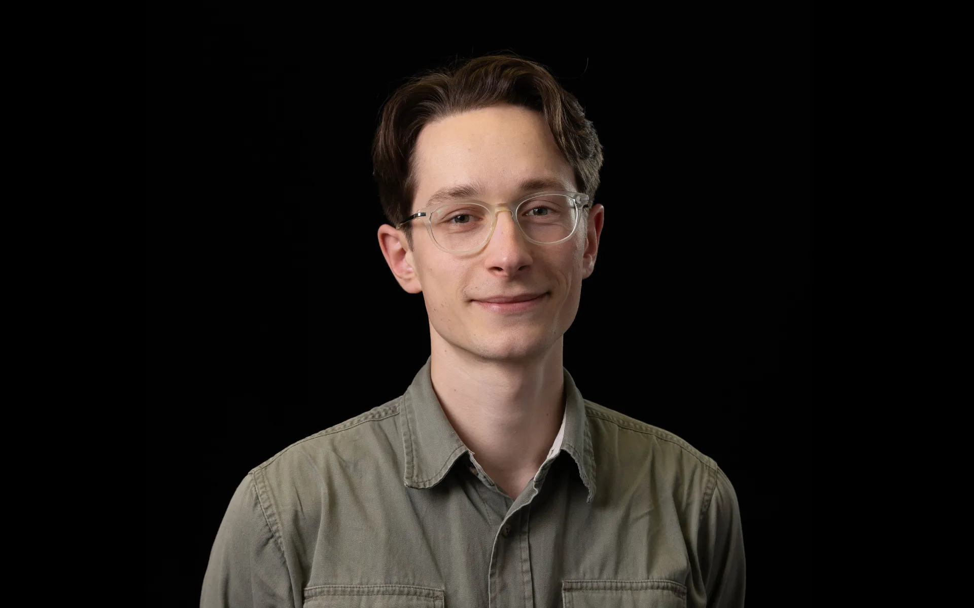 Portrait of Sandy Buchan wearing glasses and an olive-green shirt against a black background.