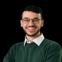 A headshot of Asad Ibn Saifullah wearing a green jumper over a white shirt