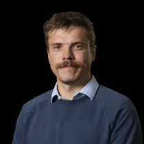 A headshot of Jack Rigby wearing a blue jumper over a blue shirt
