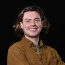 A headshot of Joe Barry wearing a brown overshirt and a grey t-shirt