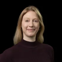Portrait photo of Sarah smiling at the camera, wearing a dark polo neck top.