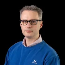A headshot of Aaron Southwood wearing glasses and a blue jumper.