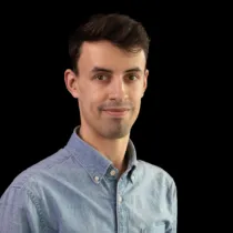 Studio portrait of a man wearing a light blue button-down shirt, photographed against a black background.
