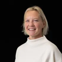 Photo of person with blonde hair, wearing a white high-necked top, against a black background.