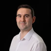 A portrait of Alec wearing a white shirt against a black background.