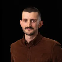 A portrait of Andrew Terry wearing a dark brown shirt against a black background.