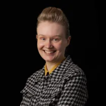 Portrait of Brooke Smith wearing a checked shirt against a black background.