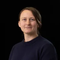 Portrait of Chloe Hurley wearing a navy jumper against a black background.