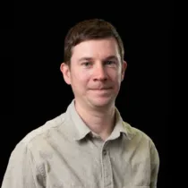 Portrait of David Leonard wearing a beige shirt against a black background.