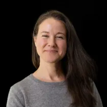 Portrait of Gill Pyatt wearing a grey jumper against a black background.