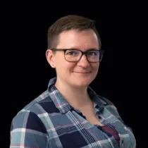 Portrait of Heather McCready wearing glasses and a blue checked shirt against a black background.