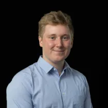 Portrait of Iain Nethercote wearing a light blue button-up shirt and glasses against a black background.